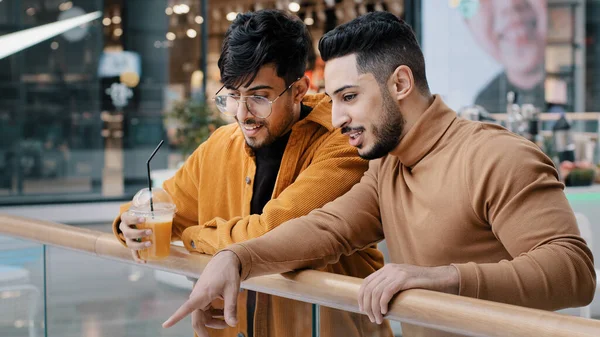 两个积极的阿拉伯男孩朋友学生站在商场和娱乐中心的公共场所聊天交流 指指点点 选择在哪里可以享受周末时光的男人喝果汁 — 图库照片