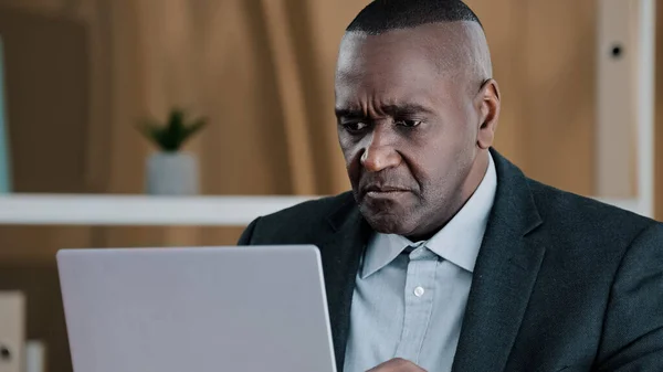 Upset frustrated African American adult old senior mature businessman elderly citizen man looking in laptop screen with sad lost failure suddenly female hands give money dollars banknote finance prize