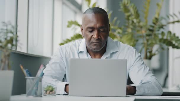Concentrated african man employee american expert focused specialist sits in office works on laptop use personal computer typing email chatting analyzing financial data pay internet order e-commerce