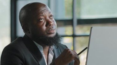 Doubtful thoughtful african american team leader male coach think question solve daily working task in mind has dilemma self brainstorming reflective turns pen by hand create project business strategy