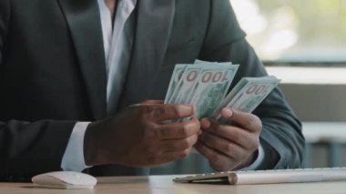 Unknown rich wealthy african businessman investor entrepreneur bookkeeper cashier banker counting money earnings salary hundred dollars banknotes winning lottery monetary prize getting deposit in bank