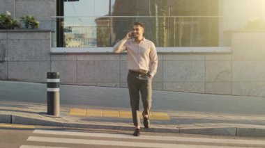 Adult busy successful businessman walking in city street on road way answer call with smartphone remote distant negotiation talking on mobile phone conversation crosses going pedestrian crossing walks