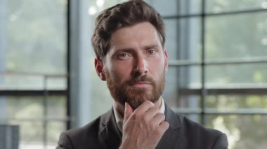 Pensive adult Caucasian bearded man 40s businessman posing looks around thinks pondering pensive thoughtful thinking about job project problem solutions comes up with ideas raised finger up in office