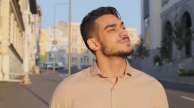 Portrait headshot close up pensive thoughtful dreaming inspired calm mindfulness Arabic Latin Indian bearded businessman guy man standing in city street enjoying resting fresh air looking in sky dream