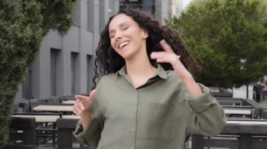 Successful funny winner lucky female lady with long curly hair playing with curls woman girl waving head dancing to music outdoors celebrating having fun at weekend in city businesswoman dance moving