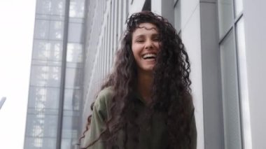 Closeup funny happy smiling laughing cheerful female lady with long curly hair hairdo haircut playing with curls jumping in air woman girl jump outdoors celebrating having fun posing looking at camera