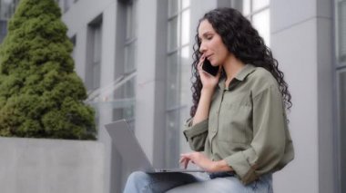 Busy multitasking businesswoman user freelancer worker lady sitting outdoor outside talking mobile phone typing laptop answer call ordering booking ecommerce shopping online with wireless computer app