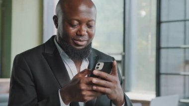 African american adult businessman bearded male employee chatting in cell app hold mobile phone upload business information scroll internet pages make online order booking tickets read digital content