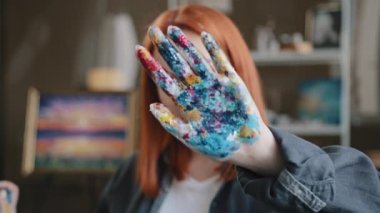 Female calm red-haired girl artist lady Caucasian 30s woman painter designer holding hand in front stop gesture not no gesture showing dirty in acrylic paint palms looking at camera in art studio