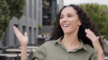 Close up happy cheerful funny female 30s woman with curly long hair dancing singing having fun outdoors moving active to music celebrate dance in city girl with gorgeous hairstyle enjoy good mood