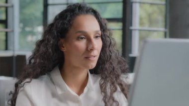 Close-up young hispanic woman professional manager working in office on computer attractive female programmer checking software looking at camera showing ok sign approval gesture excellent good result