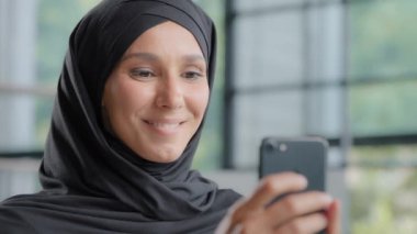 Close-up positive arab woman in hijab holding phone making order in online store friendly smiling muslim female consultant responding to client in web chat using smartphone chatting with friend remote