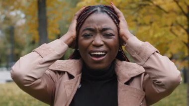 Close-up worried anxious young woman standing outdoors shouting loudly in rage covers ears with palms from noise annoyed frustrated girl feels stress hopelessness holding head suffering from headache