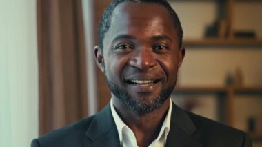 Male portrait adult successful african american businessman posing indoors joyful positive man client looking at camera smiling winking with one eye flirting recommending services advertises product