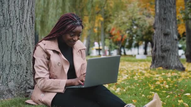 Ενθουσιασμένη Αφροαμερικανή Γυναίκα Που Κάθεται Στο Πάρκο Φθινόπωρο Παίζοντας Online — Αρχείο Βίντεο