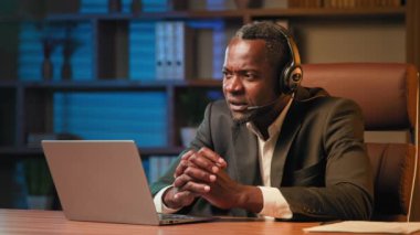 Office worker in headphones communicates with client on headset on laptop male psychologist talking to patient via video call at online conference businessman conducts remote negotiations on webcam