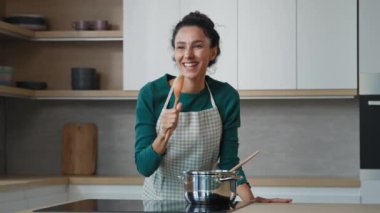 Playful funny arabian housewife maid artistic woman having fun party at home in modern kitchen dancing rhythmic moving to energetic music singing song in culinary spoon microphone feeling as pop star