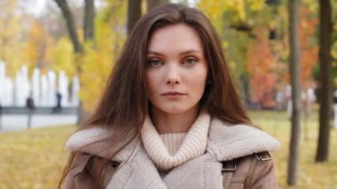 Close up female headshot portrait beautiful serious caucasian european appearance with flawless clean skin woman brunette millennial 20s girl upset offended lady stand in autumn park outdoors posing