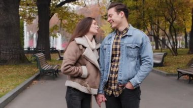 Happy young lovers caucasian couple cheerful family spend time together in autumn park walk street hold hands dreaming about future pleasant talking brunette girlfriend lovely flirting with boyfriend