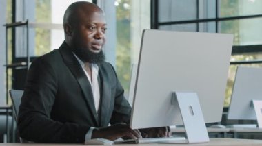 Happy african american businessman adult worker typing on laptop working remotely turn to camera smiling make approval good sign well done excellent result ok hand gesture agree recommend computer app