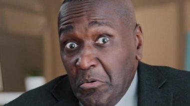 Close up front view male wrinkled elderly face emotional funny frightened puzzled African business man looking at camera feeling shock fright disgust surprise shake head no disagree fear reaction