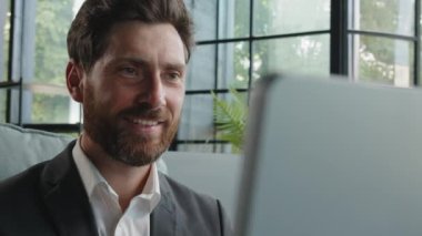 Happy dreaming smiling Caucasian bearded adult 40s man work with computer online write article looking away dreaming thinking pondering business strategy plan smile satisfied typing laptop in office