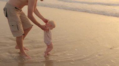 Caring father Caucasian dad holds little daughter child by hands teaches to walk helps to step on warm waves play with water together on beach near sea ocean in summer kid toddler development explore
