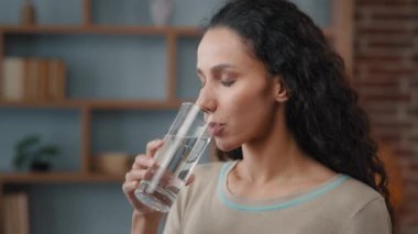 Healthy happy 30s Caucasian Hispanic woman with long hair perfect skin drinking still water at home has good habit holding glass drinking clean mineral natural h2o beverage feeling good freshness