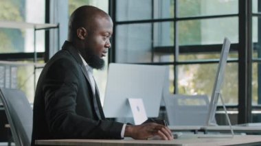 Side view african american senior businessman analyst ceo manager sit at office desk typing email chatting on corporate computer concentrated search online data e-business commerce use wifi internet