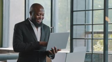 African american man developer boss 30s senior businessman investor stand in office place hold portable laptop use touchpad to click on website programming code online trading search e-commerce data