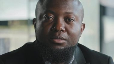 Portrait of sad african man male businessman teacher coach upset serious ethnic biracial bearded adult plus size thick guy with dark skin wears black suit sit in modern office space looking at camera