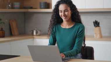 Young student arabian woman freelancer businesswoman writer shopper sit in kitchen use home internet chatting search information vacancy job on website e-commerce distant education typing on keyboard