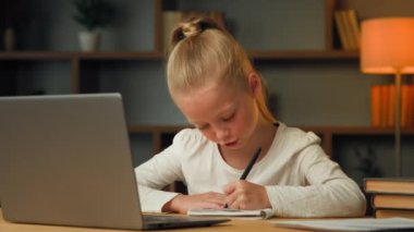 Smart pretty primary schoolgirl blonde little pupil seven years old kid studying in house room writing homework doing elementary math task imaging answer in head gesticulate making notes create ideas