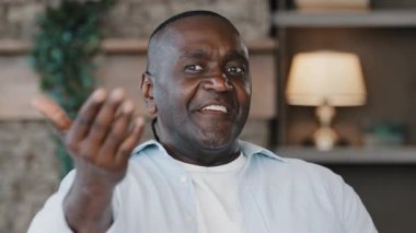 Happy hospitable african adult senior ethnic man 50s retired grandfather male asks come here allure come for visit invites to housewarming welcoming sign makes okay like hand gesture winks eye flirt