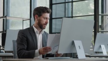 Focused business man entrepreneur employee typing on laptop doing research with documents paperwork male professional typing computer working online write information in internet website service app