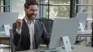 Happy Caucasian bearded businessman in office looking at computer screen with emotion winner cheerful rejoice with online win financial betting growth man worker CEO overjoyed celebrating success