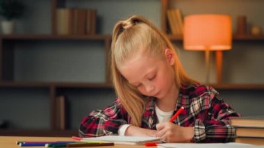 Creative caucasian blonde little girl cute child artist daughter preschool pupil sitting at table in children room kindergarten drawing picture with colored pencil enjoying art hobby painting paper
