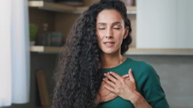 Young curly girl hispanic frank honest woman stand indoor put folded palms on chest make thankful trust gesture demonstrate belief friendly sign sincere apology devotion tenderness and charity concept