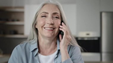 Old happy smiling woman housewife 60s grey-haired senior lady granny talk mobile phone with grandchildren family answer call booking online remotely conversation use telephony communication share news