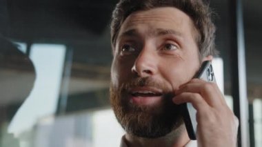 Extreme close up smiling bearded 40s adult professional businessman making business call with smile talking phone indoors happy salesman enjoying mobile conversation remote talk distant communication