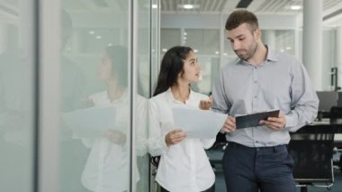 Young colleagues communicate in modern office discuss work plan on sales compare data share information diverse employees corporate agency having friendly conversation talk creating startup strategy