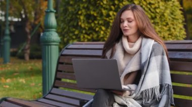 Young caucasian girl businesswoman beautiful girl sit in autumn park chatting with boyfriend on laptop online video call remote communication talking in chat use computer outdoors distant negotiation
