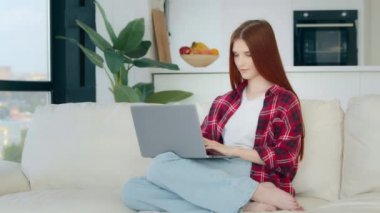Young student caucasian freelancer housewife in casual clothes plaid short businesswoman girl sits on sofa search job vacancy in internet check email message pay bills online self-education e-learning