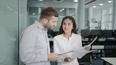 Excited Indian young businesswoman holding papers talking about benefit of offer shares impressions with male colleague explains plan for beneficial deal talks about creation new interesting project