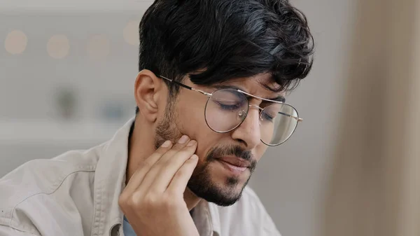 Close-up sick indian man in glasses male sad hispanic arab bearded man suffering tooth pain. Portrait guy feels toothache discomfort in gum caries holdong check with hand dental oral problem concept