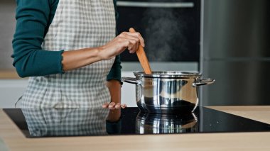 Unknown housewife mistress maid wife mom wears apron prepare food on kitchen surface electric oven cooking aromatic dish boil off soup aromatic borsch by cookery recipe stir porridge with wooden spoon