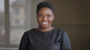 Çift ırklı, mutlu, kısa saçlı, gülümseyen bir kız. Evet, Afro-Amerikalı bir kadın kamera desteğine bakıyor.