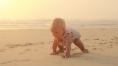 Mutlu Kafkasyalı küçük bebek kumsal kıyısında dizlerinin üzerinde sürünüyor. Küçük bir kız çocuğu, küçük bir kız çocuğu emeklemeyi öğreniyor. Okyanus kıyısındaki sahilde yürümeyi öğreniyor.