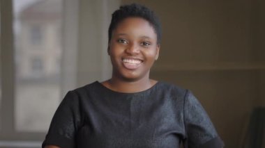 Afro-Amerikalı kız içeride gülümseyerek kalp şeklini gösteren kameraya bakıyor. Parmakları sevgiyi gösteriyor. Gönüllü bayanı destekliyor.