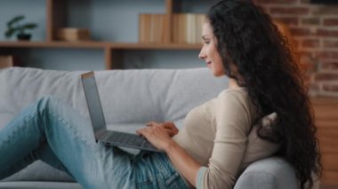 Yan görünüm gülümseyen yazar serbest yazar kadın evinde oturup dizüstü bilgisayarda klavye yazıyor arkadaşlarıyla online bilgisayar uygulaması web sosyal ağında sohbet ediyor ve uzak mesafelere çalışıyor.